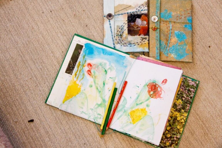 שתי מחברות על שולחן, מחברת אחת פתוח העם ציורים עליה, עפרונות מונחים על גביה.